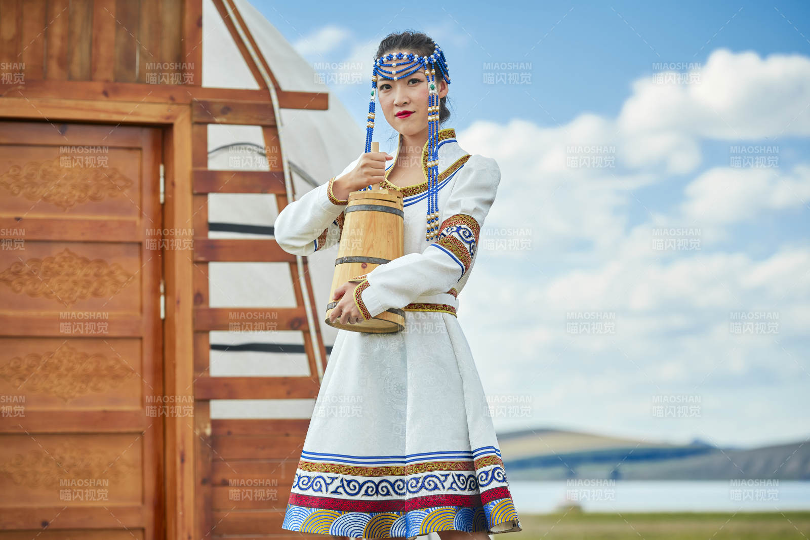 蒙古包前穿蒙古族飾懷抱奶茶桶的蒙族少女