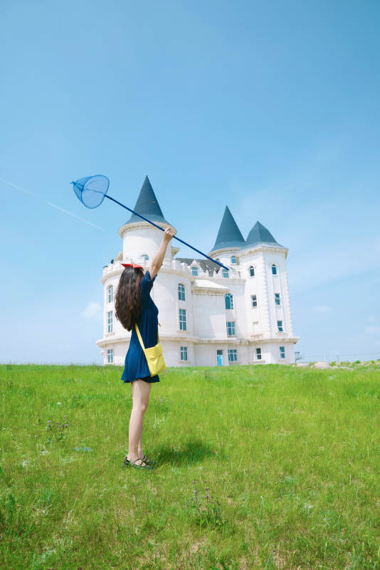 身穿小魔女服饰在城堡前拍照打卡的亚洲美女