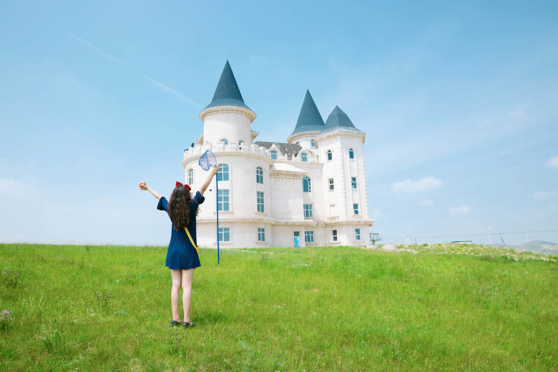 身穿小魔女服饰在城堡前拍照打卡的亚洲美女