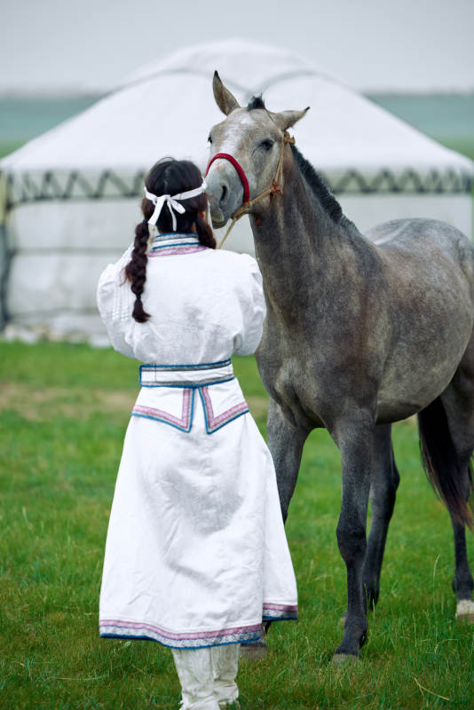 草原上穿着蒙古族服饰牵着马匹的亚洲美女