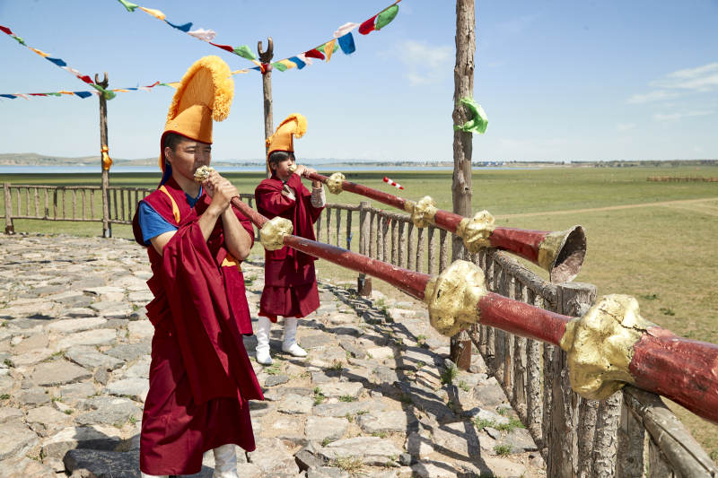 在敖包上吹响铜号的喇嘛僧人