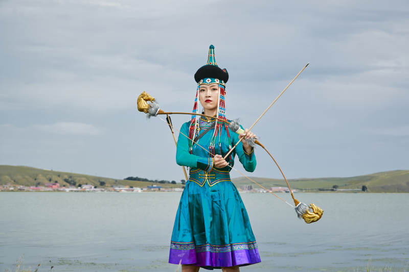 草原湖畔身穿蒙古族饰手持弓箭的蒙族少女