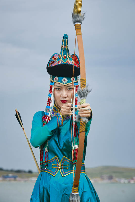 草原湖畔身穿蒙古族饰手持弓箭的蒙族少女