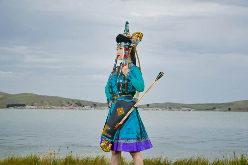 草原湖畔身穿蒙古族饰手持弓箭的蒙族少女
