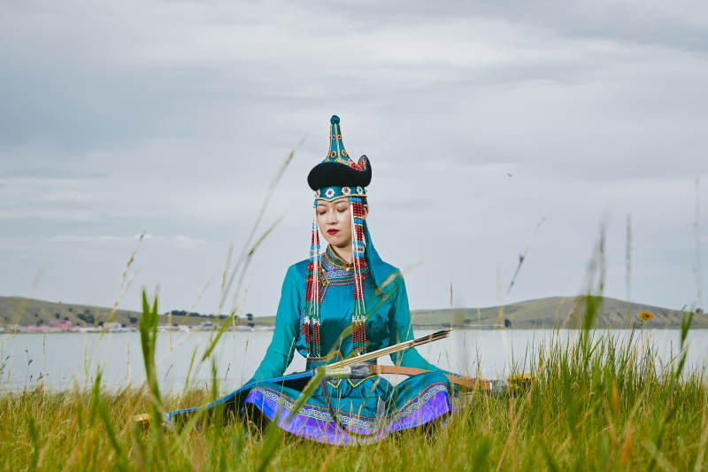 草原湖畔身穿蒙古族饰手持弓箭的蒙族少女