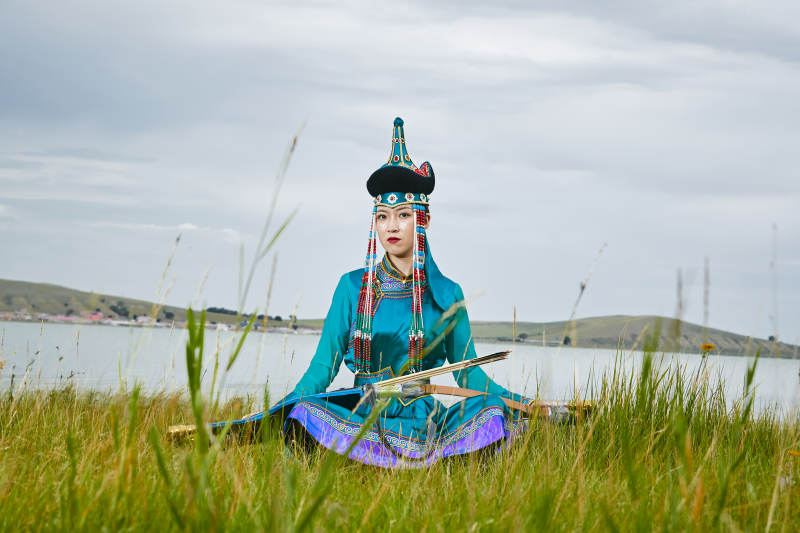 草原湖畔身穿蒙古族饰手持弓箭的蒙族少女
