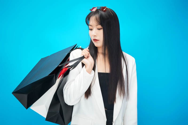 青蓝色背景下手提购物袋的亚洲时尚少女