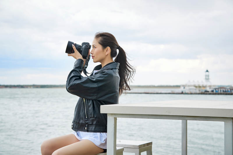 户外湖畔进行拍摄的亚洲青年女性摄影师