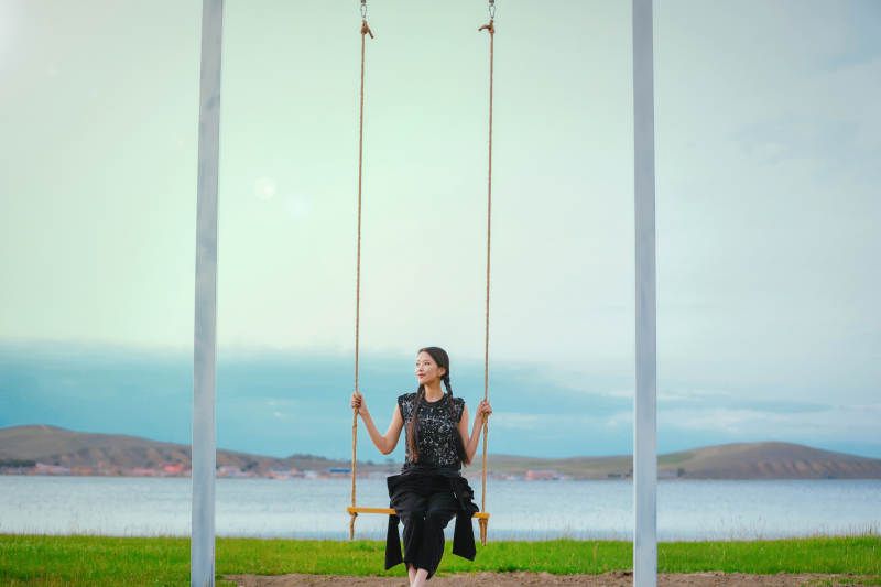 草原湖畔夕阳下荡秋千的亚洲少女