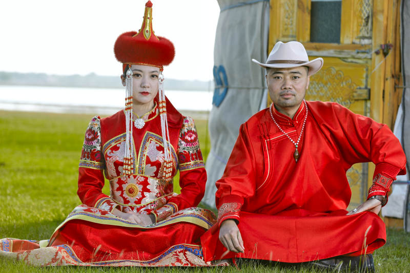 草原上蒙古包前穿蒙古族传统服饰的年轻夫妻