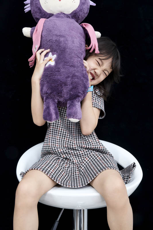 黑色背景里坐在凳子上抱着娃娃玩耍的可爱亚洲小女孩儿童