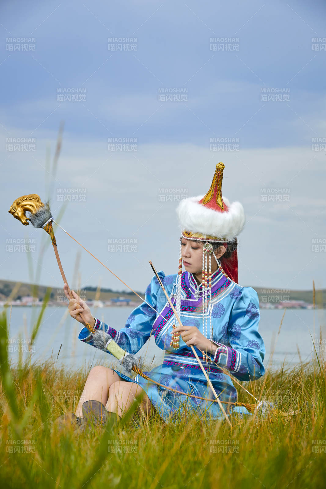 草原湖畔身穿蒙古族饰手持弓箭的蒙族少女