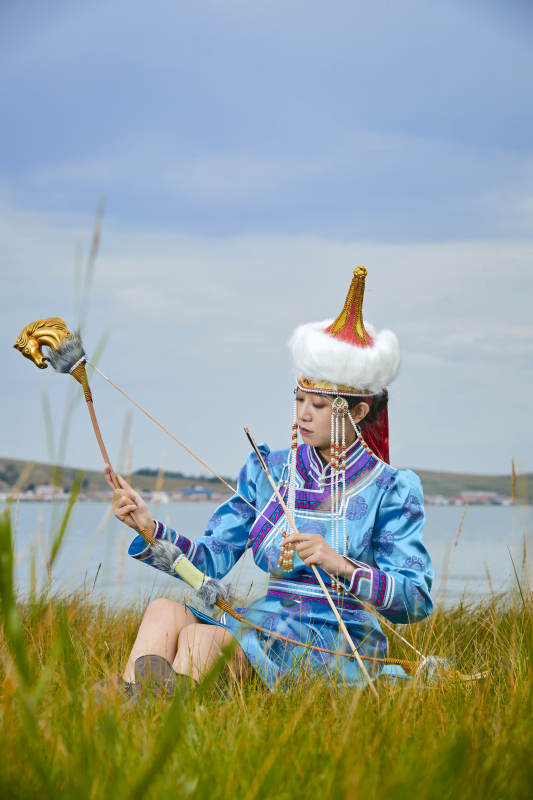 草原湖畔身穿蒙古族饰手持弓箭的蒙族少女