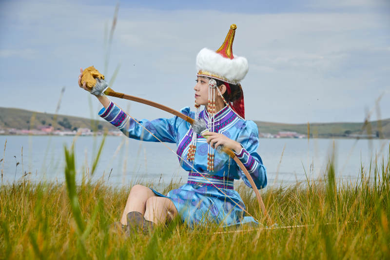 草原湖畔身穿蒙古族饰手持弓箭的蒙族少女
