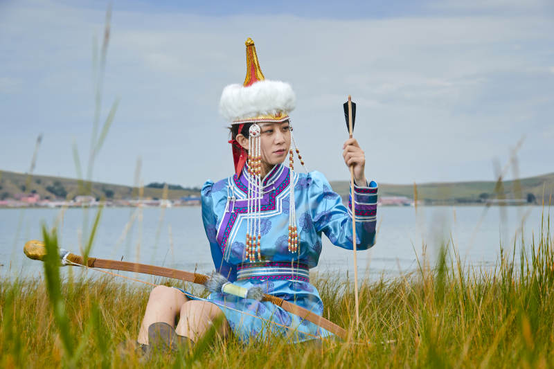 草原湖畔身穿蒙古族饰手持弓箭的蒙族少女