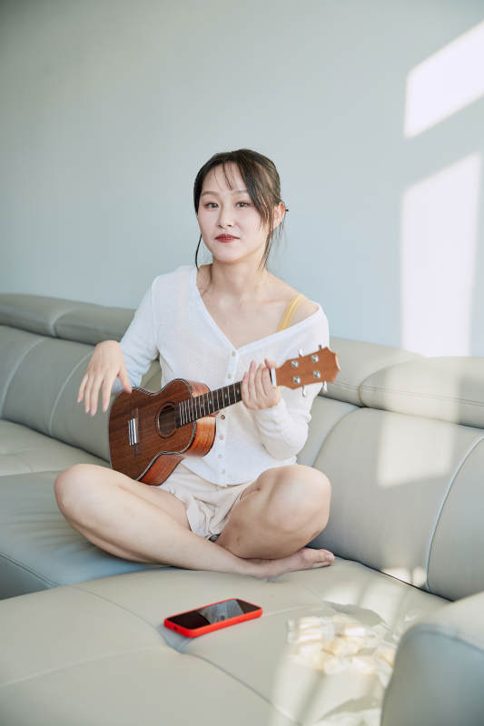 坐在沙发上弹奏尤克里里的少女