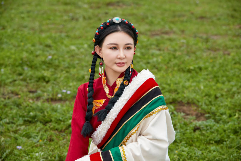 身穿红色藏族服饰在草原景区拍照的美女