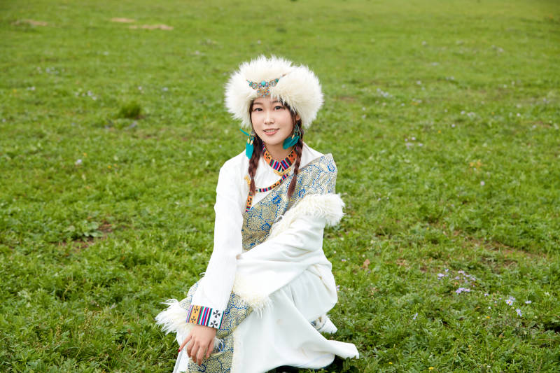 穿白色藏族服饰在草原拍照的少女