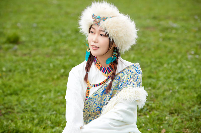 穿白色藏族服饰在草原拍照的少女