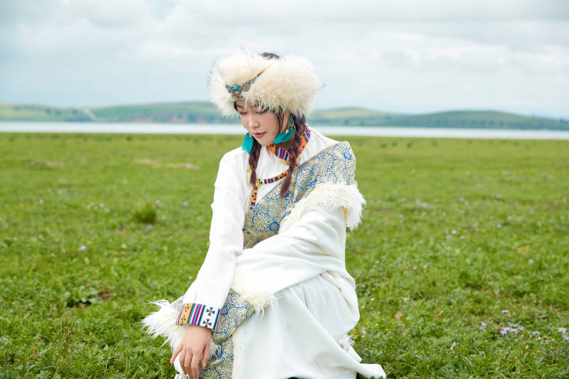 穿白色藏族服饰在草原拍照的少女