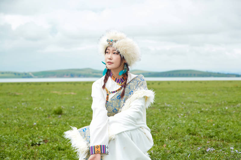 穿白色藏族服饰在草原拍照的少女