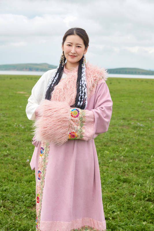 身穿粉色藏族服饰在草原拍照的少女
