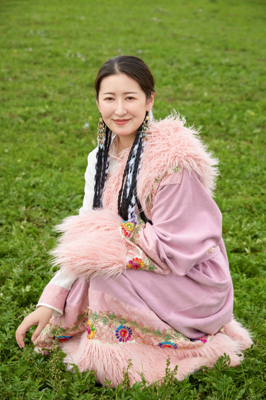 身穿粉色藏族服饰在草原拍照的少女