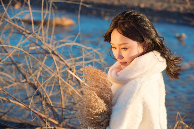 秋天在夕陽下的原野河邊拍照的美女