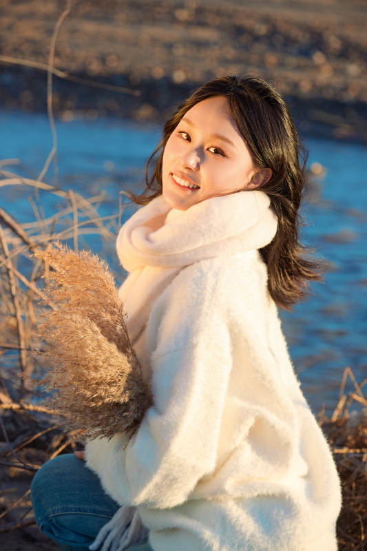 秋天在夕陽下的原野河邊拍照的美女