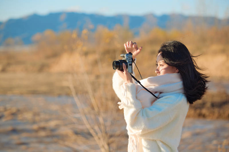 拿着相机的美女摄影师在深秋的户外拍摄