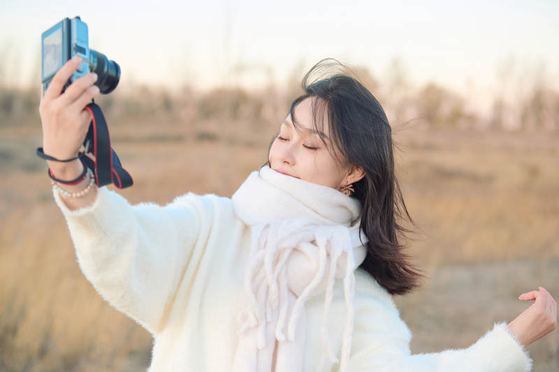 秋天夕阳下手持相机自拍的亚洲美女