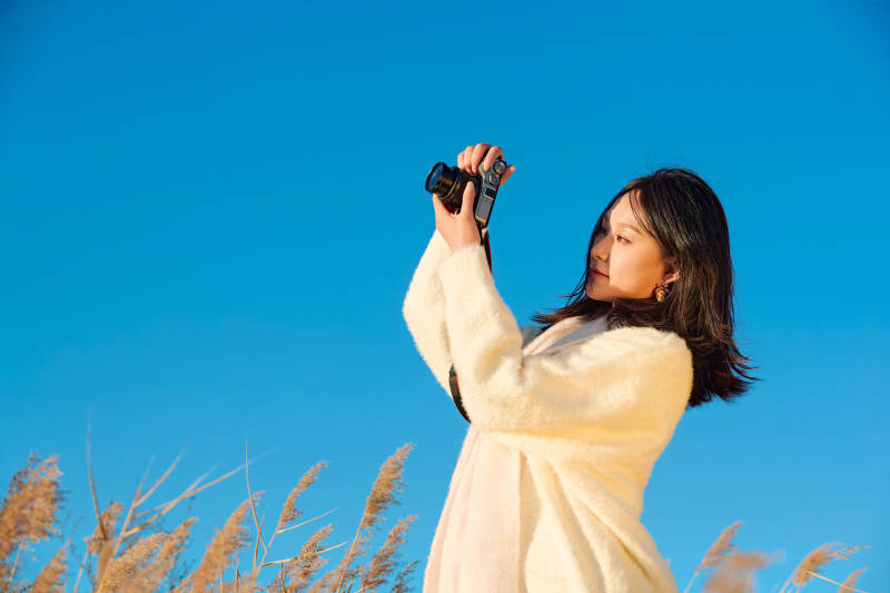 秋天晴朗的午后在芦苇荡里拍照的女性摄影师