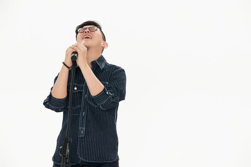 白色背景下站在麦克风前唱歌的亚洲男性