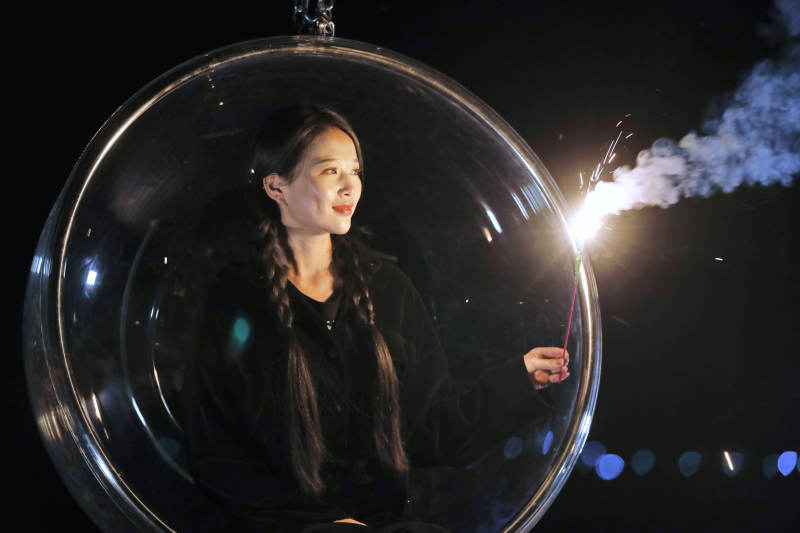 夜晚坐在透明秋千上燃放仙女棒的可爱少女