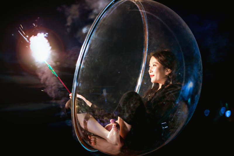 夜晚坐在透明秋千上燃放仙女棒的可爱少女