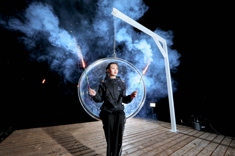 夜晚坐在透明秋千上燃放仙女棒的可爱少女