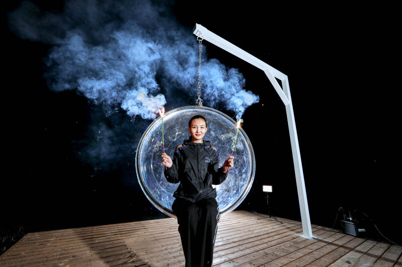 夜晚坐在透明秋千上燃放仙女棒的可爱少女