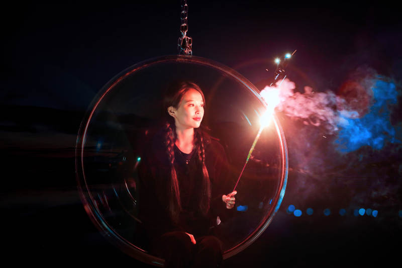 夜晚坐在透明秋千上燃放仙女棒的可爱少女