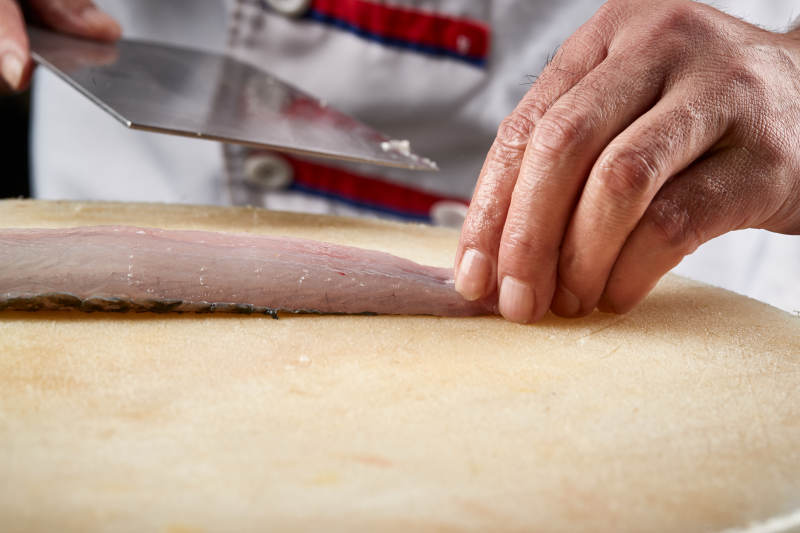 白色砧板上厨师用精湛的刀工展示生鱼片及鲜鱼料理切割分切的刀工