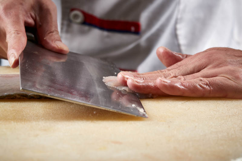 白色砧板上厨师用精湛的刀工展示生鱼片及鲜鱼料理切割分切的刀工