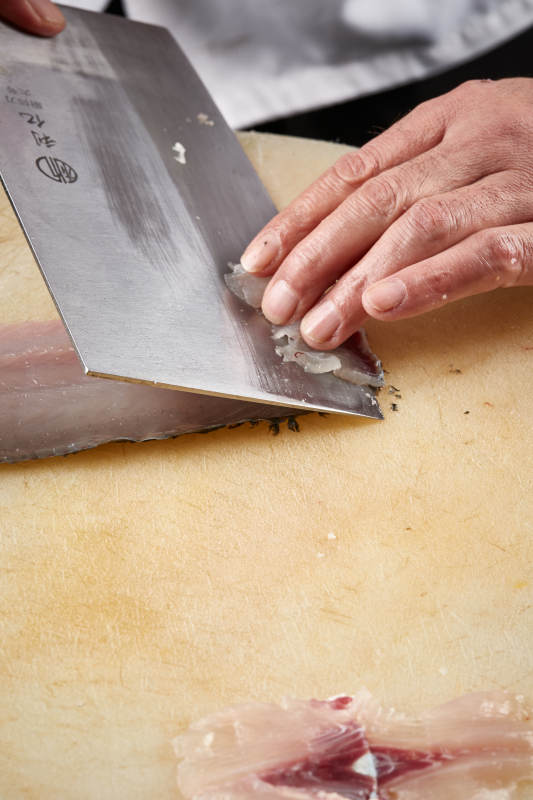 白色砧板上厨师用精湛的刀工展示生鱼片及鲜鱼料理切割分切的刀工