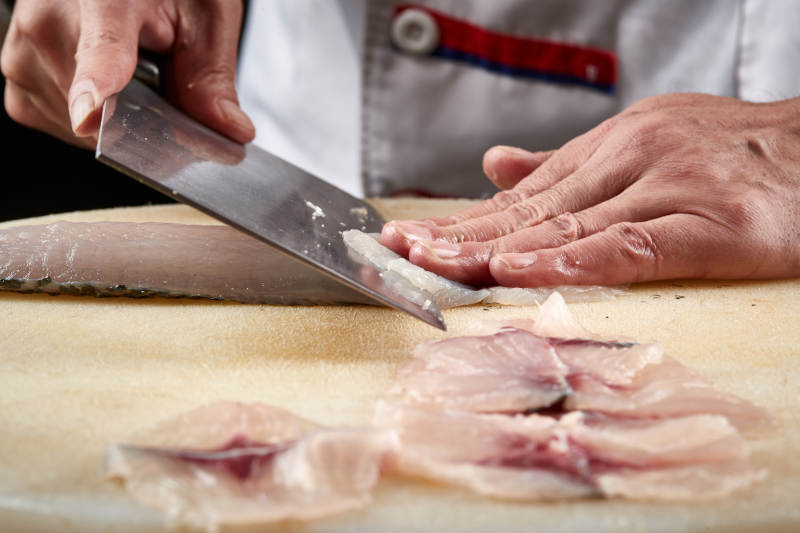 白色砧板上厨师用精湛的刀工展示生鱼片及鲜鱼料理切割分切的刀工