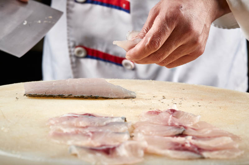 白色砧板上厨师用精湛的刀工展示生鱼片及鲜鱼料理切割分切的刀工