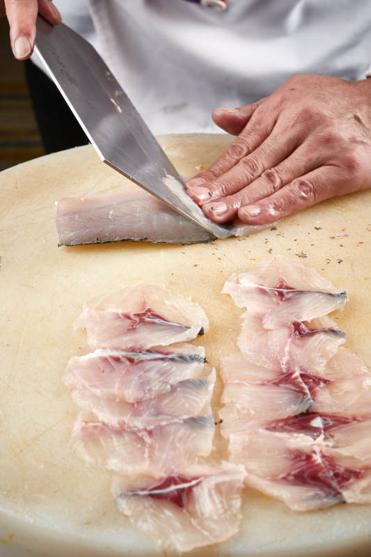 白色砧板上厨师用精湛的刀工展示生鱼片及鲜鱼料理切割分切的刀工