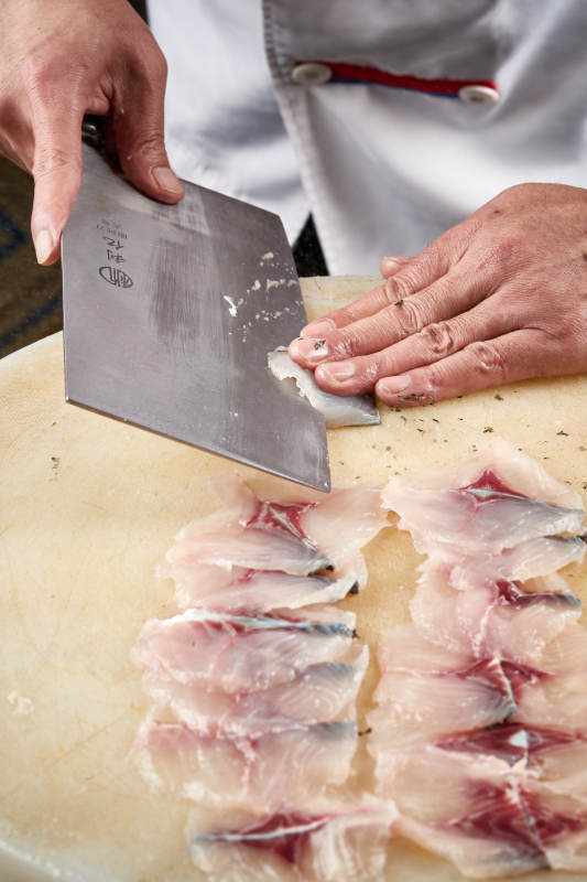 白色砧板上厨师用精湛的刀工展示生鱼片及鲜鱼料理切割分切的刀工