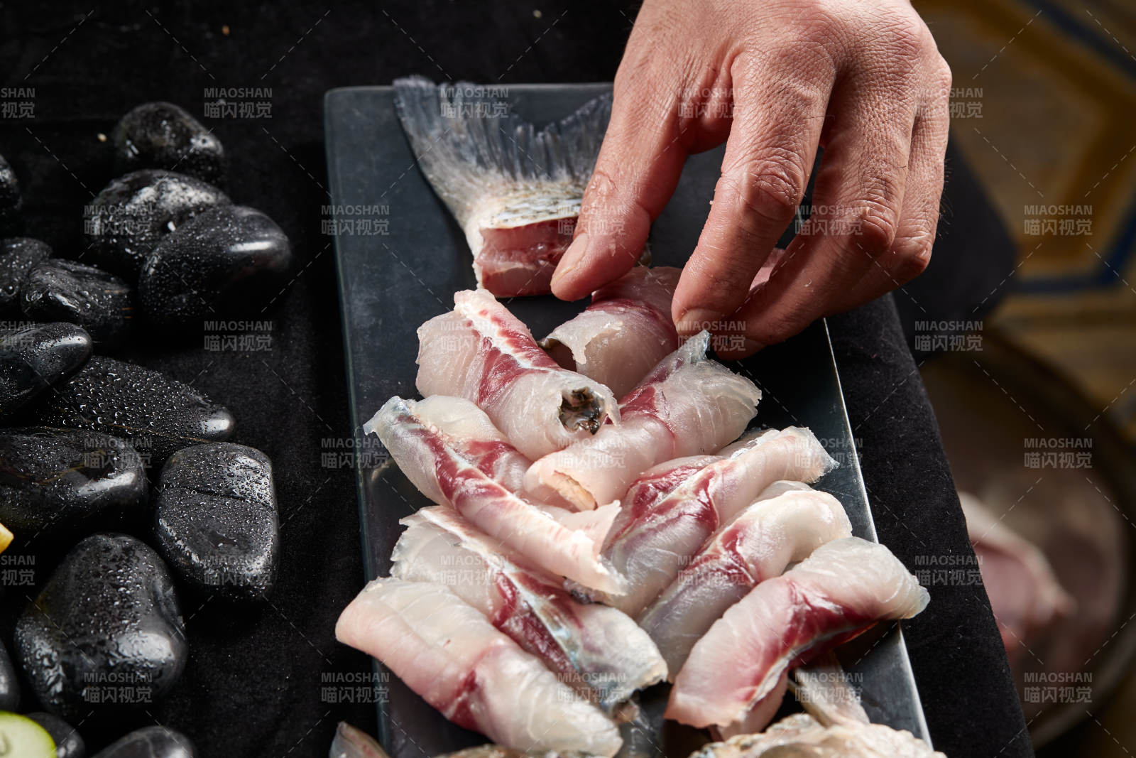 将晶莹白润的鲜鱼片码放在黑色的圆瓷盘上