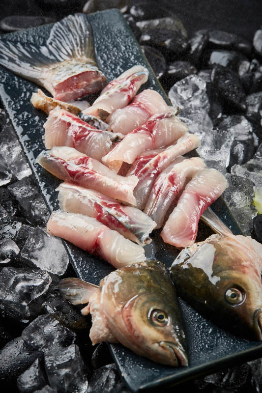 将晶莹白润的鲜鱼片码放在黑色的圆瓷盘上