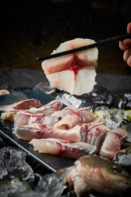 将晶莹白润的鲜鱼片码放在黑色的圆瓷盘上