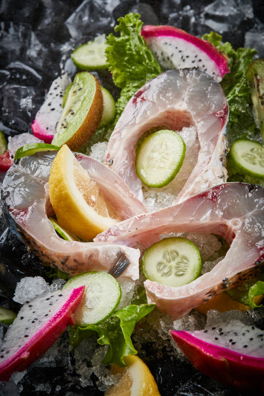 将晶莹白润的鲜鱼片码放在黑色的圆瓷盘上