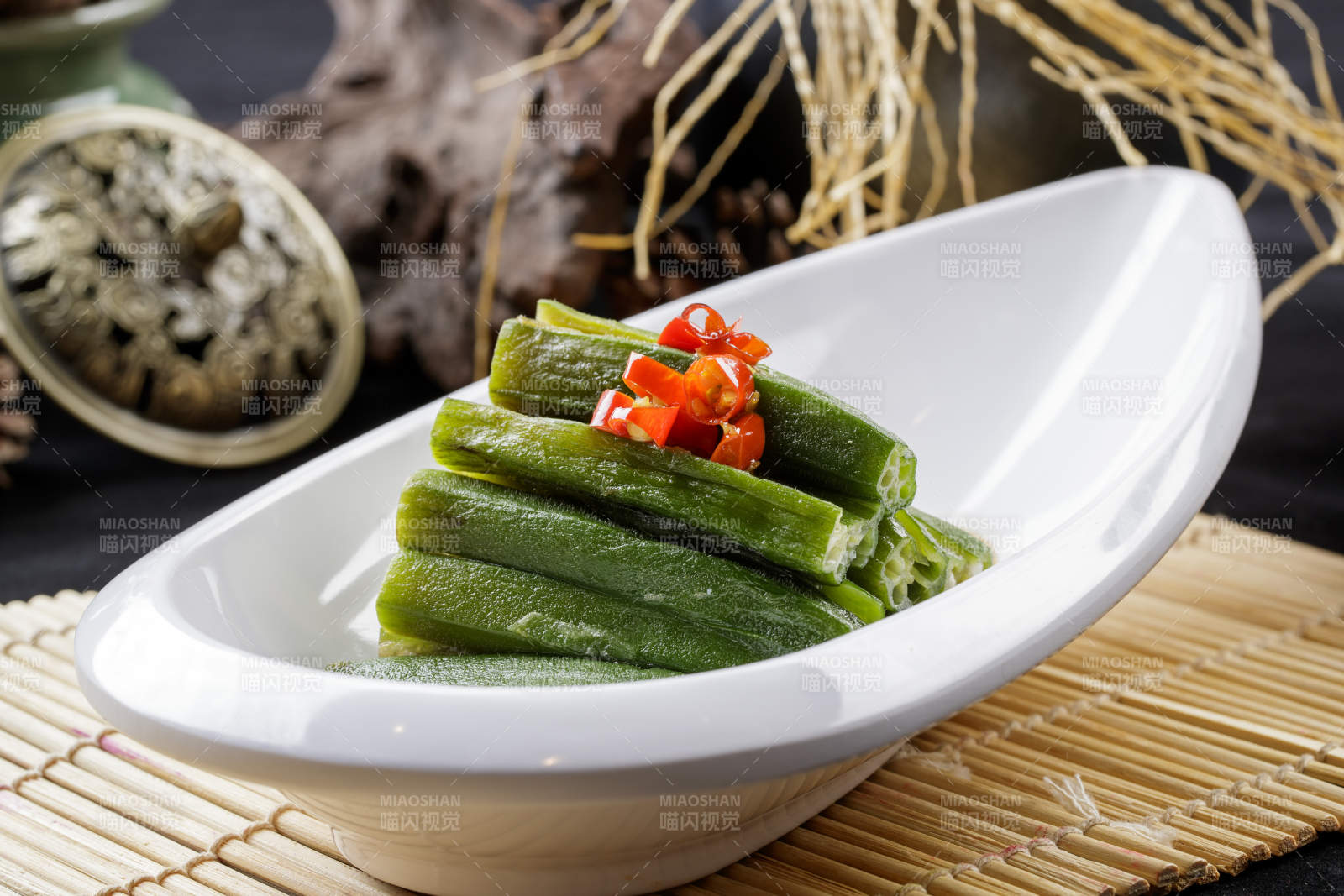 寿司帘上的元宝形瓷盘装的浇汁秋葵-摄影图